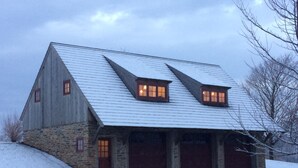 A stone barn with a sloped roof, two windows with lights, and a garage.