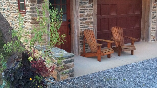 A stone building with a wooden door and two wooden chairs outside.