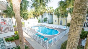A swimming pool surrounded by white fences, with lounge chairs and a small deck area.