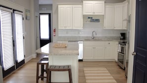 Una cocina con armarios blancos, encimera de granito, un taburete de madera y un tapete a rayas.