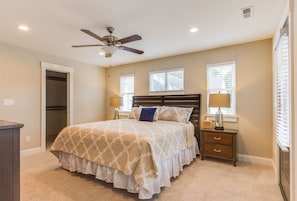 A bedroom with a bed, two bedside tables, a ceiling fan, and two windows with blinds.