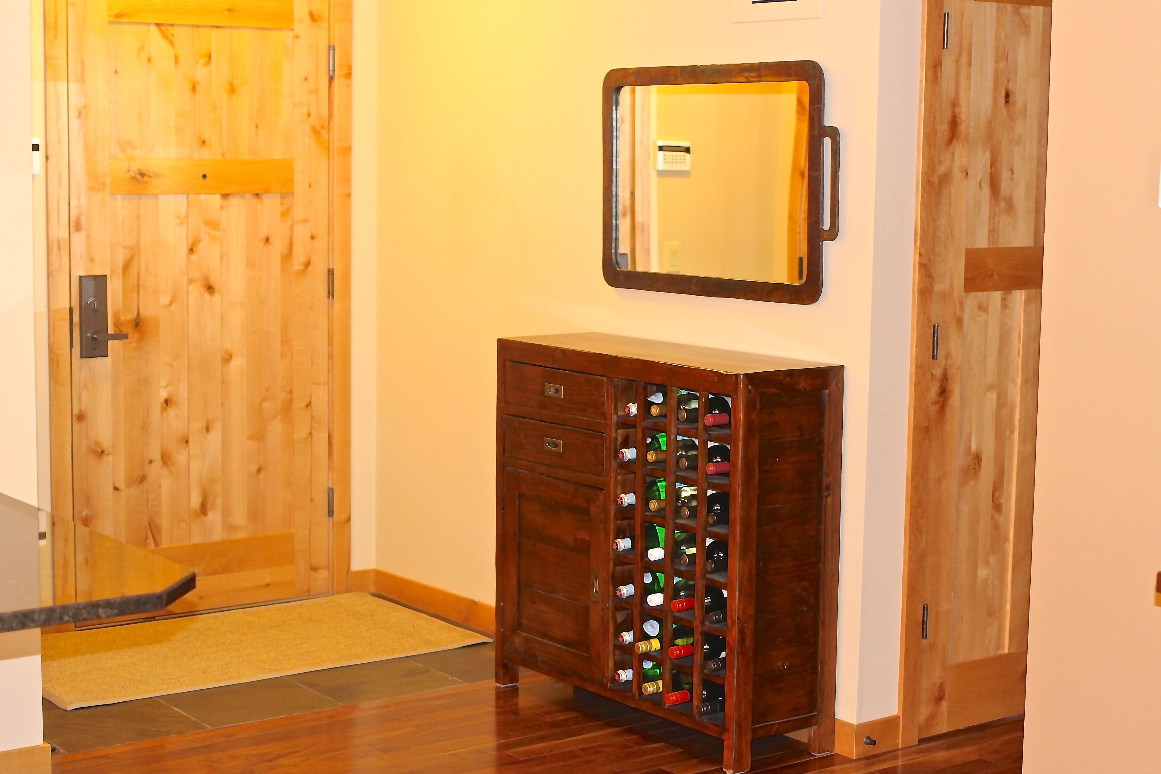 A wooden door with a mirror above it, a wooden cabinet with wine bottles, and a wooden floor.