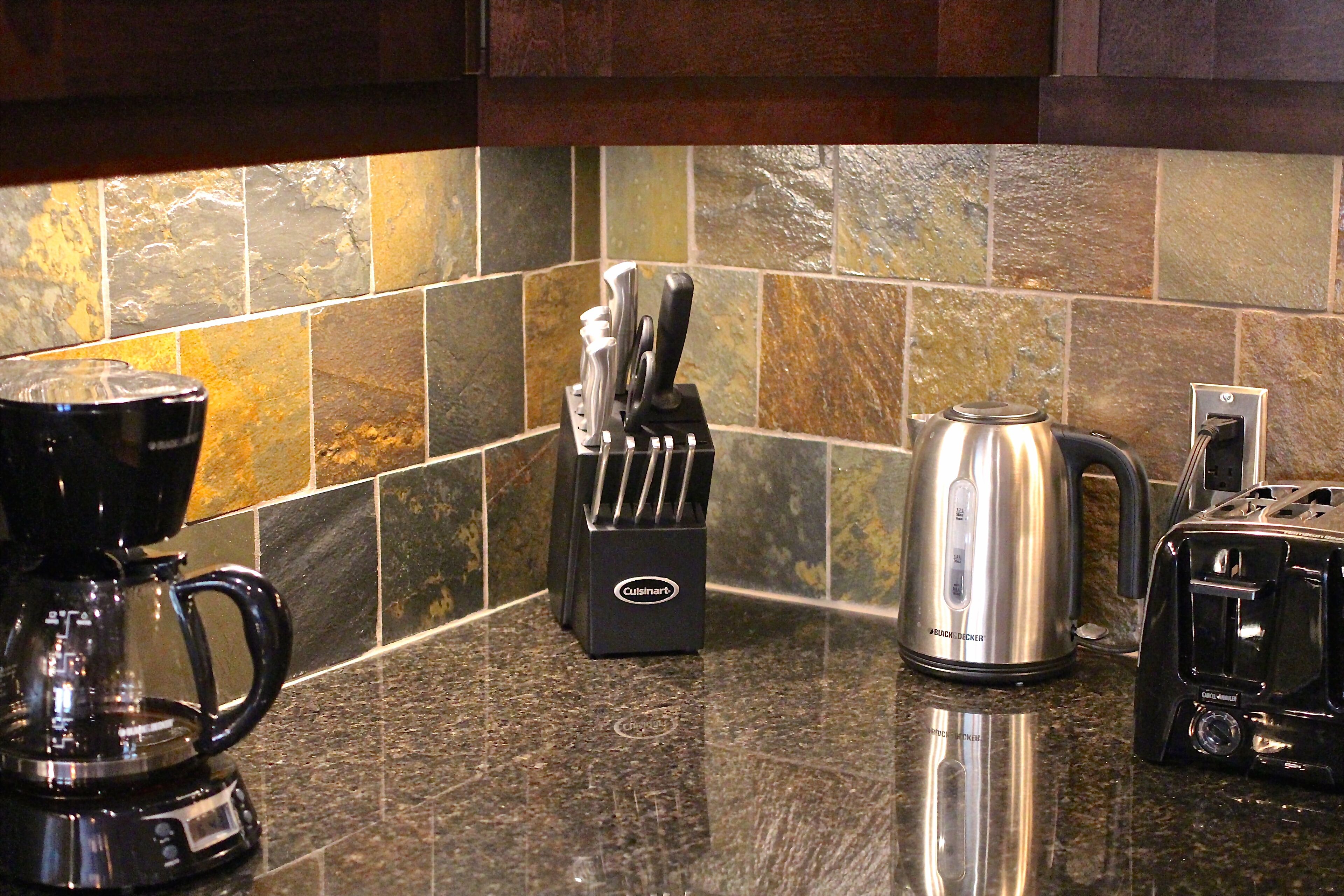 Una encimera de cocina con una cafetera, un bloque de cuchillos, un hervidor y un tostador.