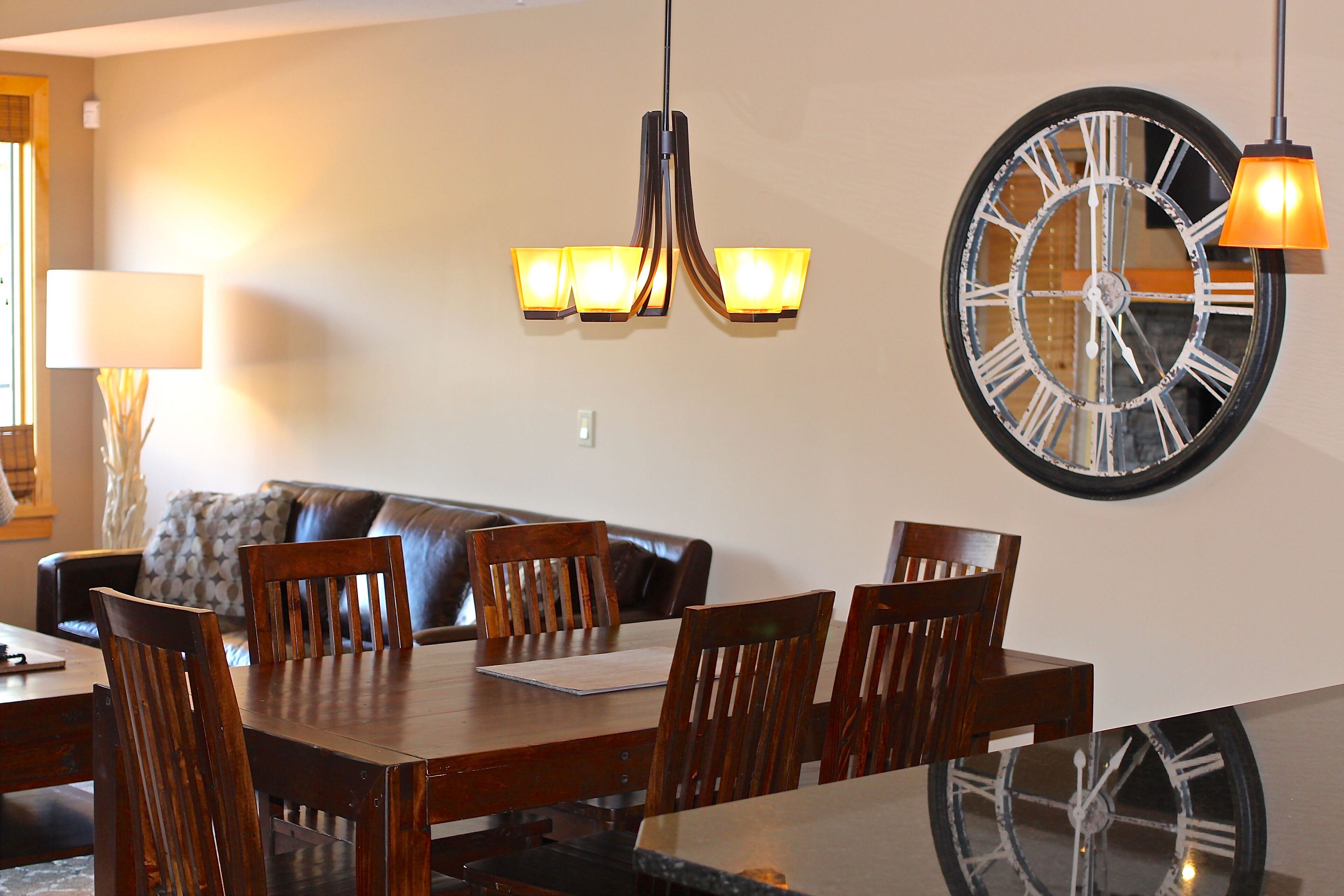 A dining area with a wooden table, chairs, a chandelier, and a large wall clock.