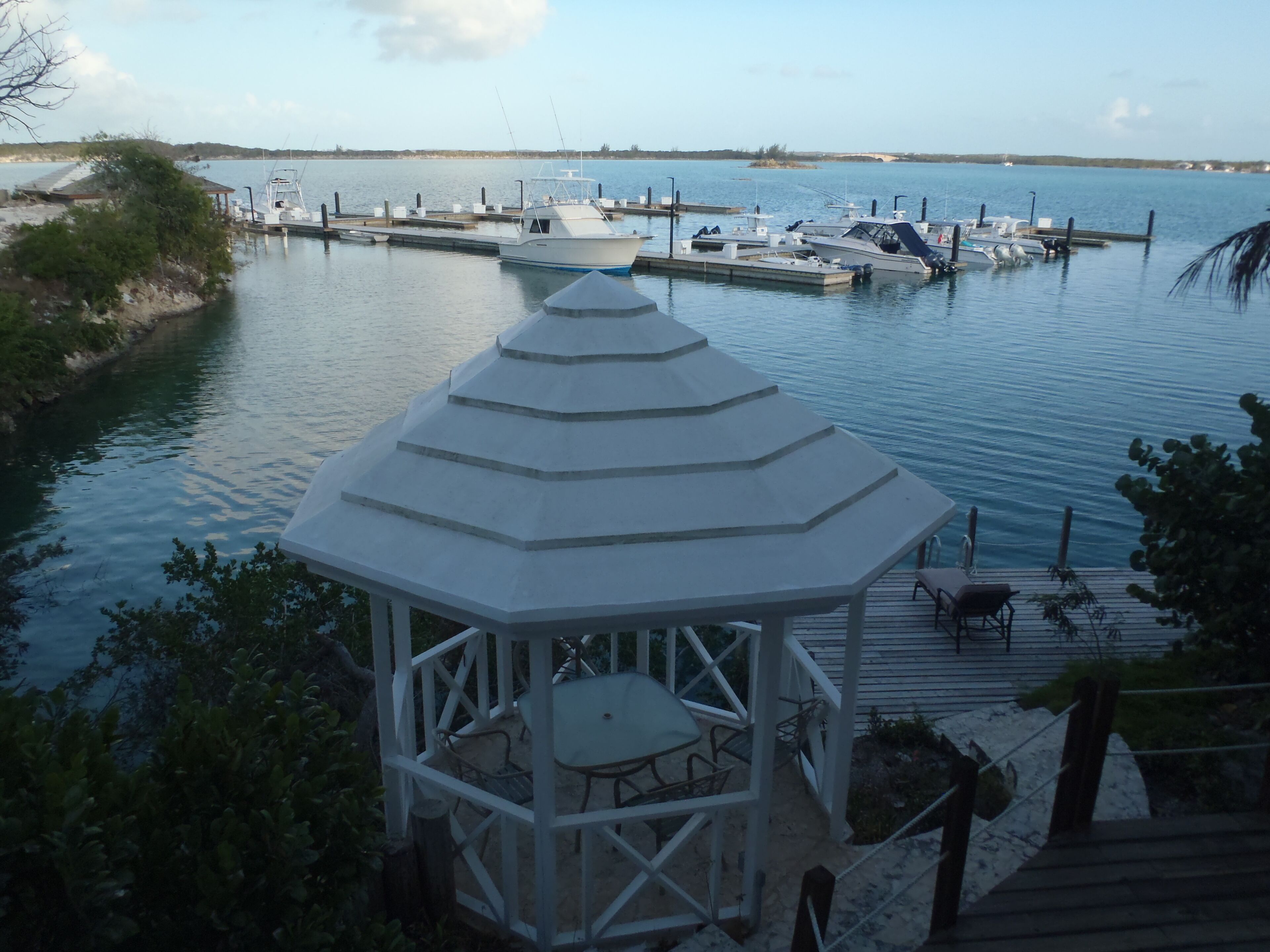 A gazebo with a table and chairs, overlooking a marina with boats docked.