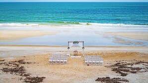 A beach wedding setup with white chairs and a wooden arch.