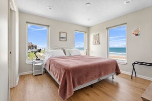 Un dormitorio con cama, mesita de noche, lámpara y vista a la playa.