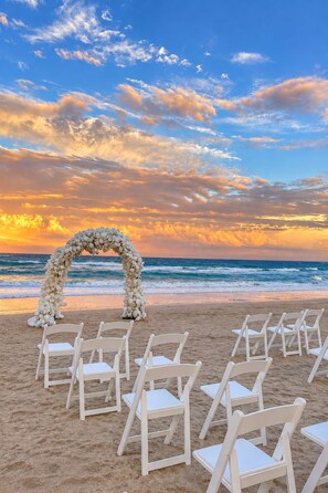 Decoración para una boda en la playa, con un arco floral y sillas blancas.