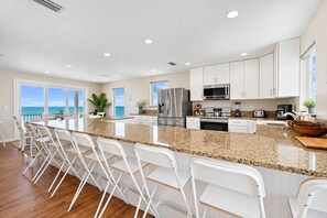 Una cocina moderna con una isla central, armarios blancos, electrodomésticos de acero inoxidable y vistas al océano.