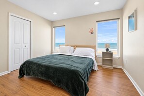 A bedroom with a bed, a nightstand, a window with a view of the beach, and a door.
