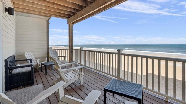 A covered deck with outdoor seating, overlooking a beach.