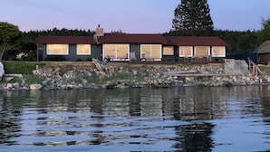 A lakeside cabin with a deck, large windows, and a stone foundation.