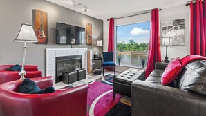 Una sala de estar moderna con chimenea, sofás de cuero rojo y negro, una silla azul y un ventanal con cortinas rojas.