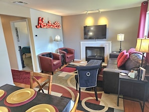 Cozy living room with a fireplace, armchairs, sofa, and TV above the fireplace. Enjoy meals at the dining table.