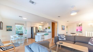 A modern living room with a grey sofa, a wooden coffee table, and a dining area with white chairs and a small table.