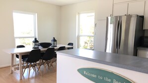 A modern kitchen with a stainless steel refrigerator, a dining table with chairs, and a 'Welcome to the Beach' sign.