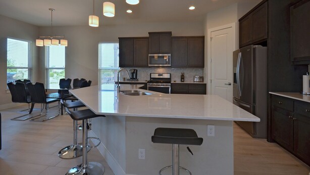 A modern kitchen with a large island, dark cabinets, stainless steel appliances, and pendant lighting. - SXSW,    FORMULA 1,     ACL,     WEDDINGS,     GRADUATIONS,    JUST FOR FUN (Round Rock)