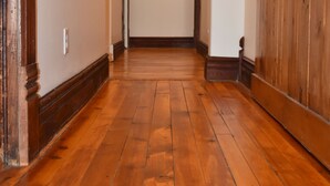 Un pasillo con suelo de madera, cuadros en las paredes y un espejo.