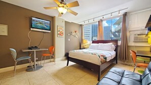 Une chambre d’hôtel équipée d’un lit, d’un bureau, d’une chaise, d’un ventilateur de plafond, d’une télévision et d’une fenêtre avec des rideaux.