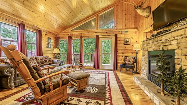 A log cabin interior with a fireplace, wooden furniture, and large windows. - H1 - Mountain Cabin-Hot Tub-1.5 miles to Dollywood-Resort Pool-No Mountain Roads (Sevierville)