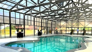 Une piscine intérieure dotée d’un toit en verre, entourée d’un espace aménagé avec des sièges et des plantes en pot.