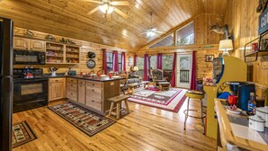 A spacious wooden cabin with a kitchen featuring a stove, microwave, and refrigerator. There are wooden cabinets, a dining table with chairs, and a bar area with stools. - H1 - Mountain Cabin-Hot Tub-1.5 miles to Dollywood-Resort Pool-No Mountain Roads (Sevierville)