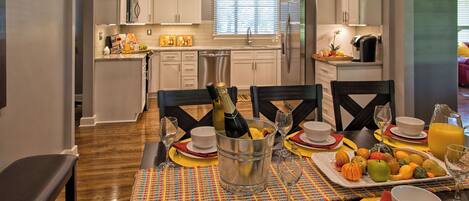 Comedor con una mesa lista para comer, cocina al fondo y una ventana con persianas.
