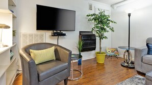 Una sala de estar con un sillón de cuero, un televisor de pantalla plana, un piano, una planta en maceta y una mesa de vidrio con un cuadro de colores.
