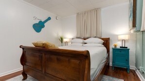 Un dormitorio con cama de madera, una mesita de noche con lámpara, una obra de arte de guitarra en la pared y un reloj fijado a la pared.