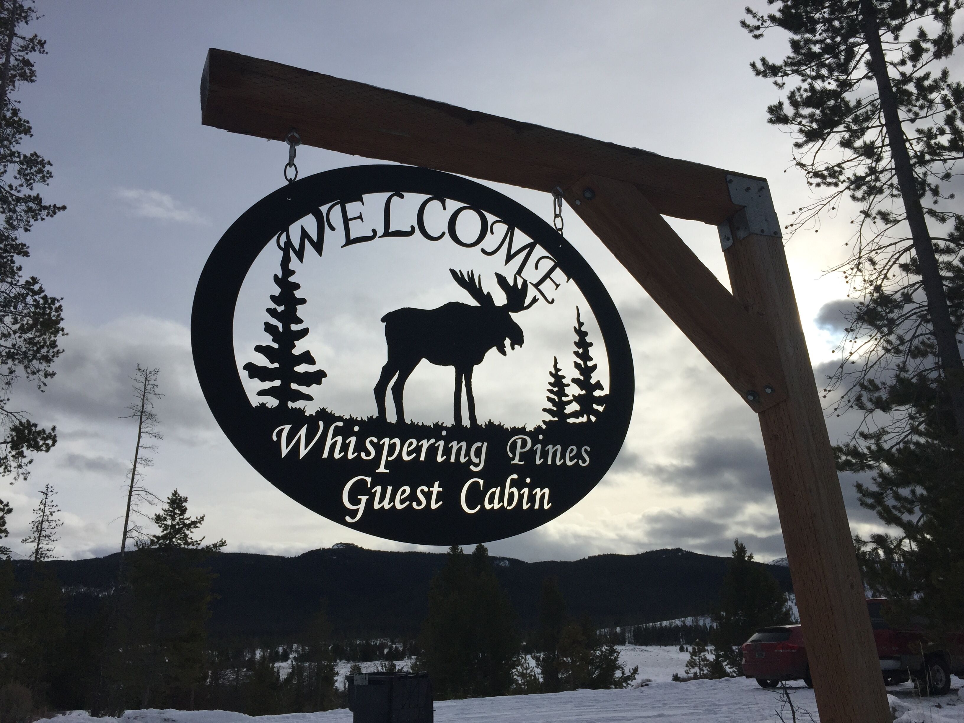 A circular sign with a moose silhouette and the text 'Welcome Whispering Pines Guest Cabin.'
