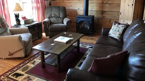 A cozy cabin interior with a wooden interior, a fireplace, a sofa, a chair, and a table.