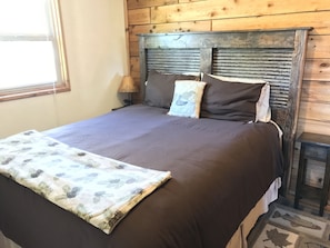 A bed with a dark brown bedspread, a quilted pillow, and a decorative pillow with a pineapple design.