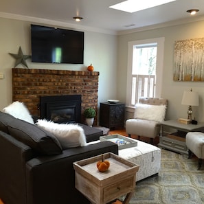 A living room with a brick fireplace, a flat-screen TV, a sofa, a chair, and a coffee table with a pumpkin decoration.