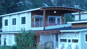 A two-story house with a balcony, a covered patio, and a front porch with chairs.