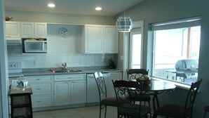 A modern kitchen with white cabinets, a microwave, a sink, and a dining area with a table and chairs.