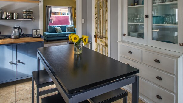 Una cocina con una mesa negra, un armario con puertas de cristal y un sofá azul al fondo.