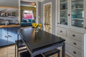 Une cuisine avec une table noire, un meuble avec des portes en verre et un canapé bleu à l’arrière-plan.