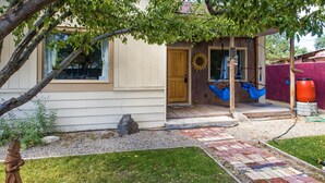 Una casa con puerta de madera, un porche con hamacas azules y un jardín con un sendero empedrado.