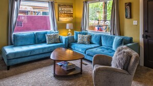Una sala de estar con un sofá azul, una mesa de centro de madera y un sillón estampado.
