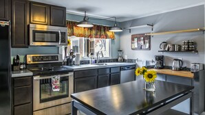 Una cocina moderna con electrodomésticos de acero inoxidable, una isla central y un ventanal con cortina decorativa.