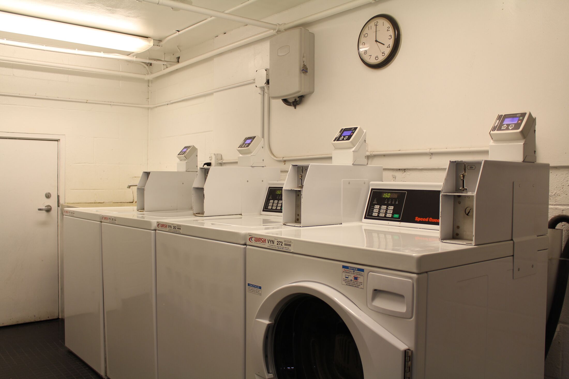 A laundry room with multiple washing machines, a clock, and control panels.