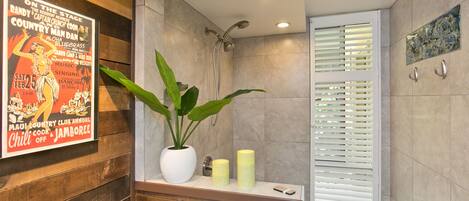 Une salle de bain avec une douche, une plante en pot, des bougies et une affiche accrochée au mur.