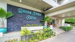 The exterior of the Waikiki Grand Hotel with a stone facade, outdoor seating area, and a sign indicating a full bar.