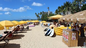 A beach with yellow umbrellas, lounge chairs, and thatched-roof stalls.