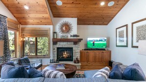 Una sala de estar acogedora con chimenea, techo de madera y un televisor mostrando un partido de golf.