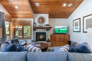 Una sala de estar acogedora con chimenea, techo de madera y un televisor que muestra un partido de golf.
