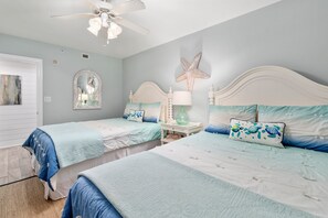 Un dormitorio con dos camas, ventilador de techo, decoración con una estrella de mar y una ventana con espejo.