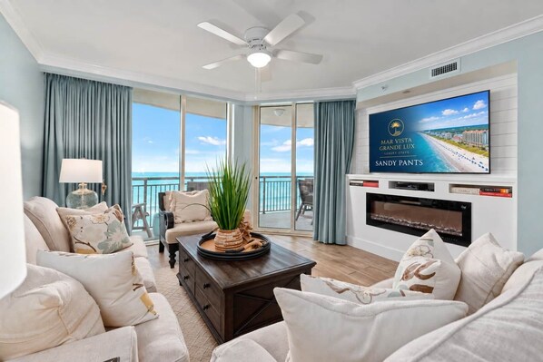 A spacious living room with a large flat-screen TV, a fireplace, and a view of the ocean.