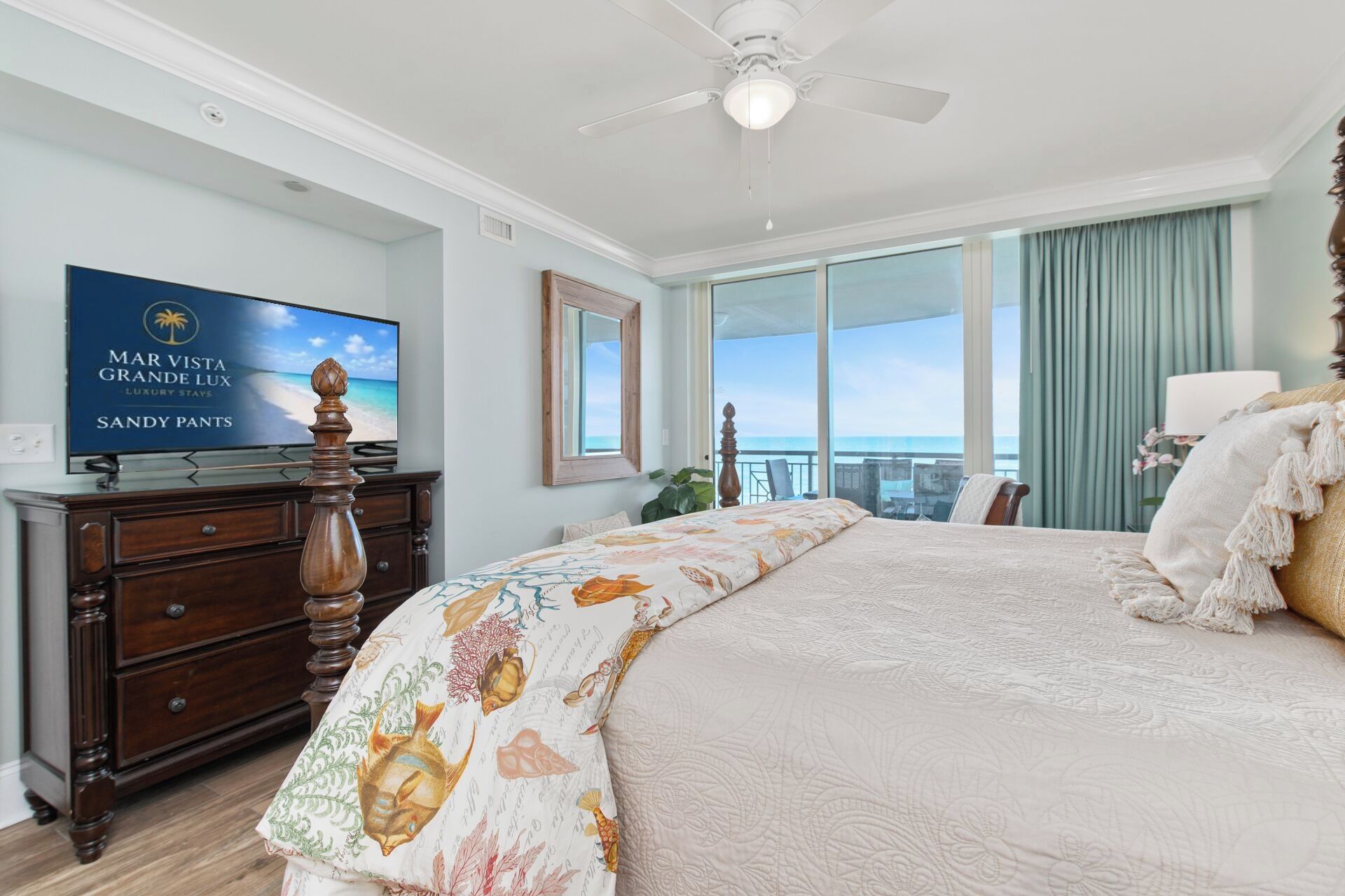 A hotel room with a bed, a television, a dresser, and a balcony with a view of the ocean.