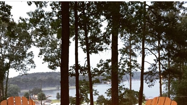 Two Adirondack chairs facing a campfire with a lake and forest in the background.